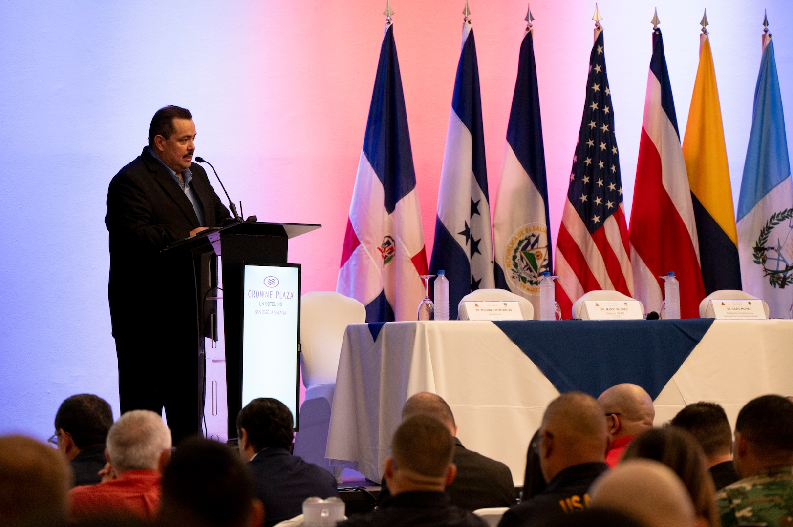 A photo of a man standing at a podium speaking.