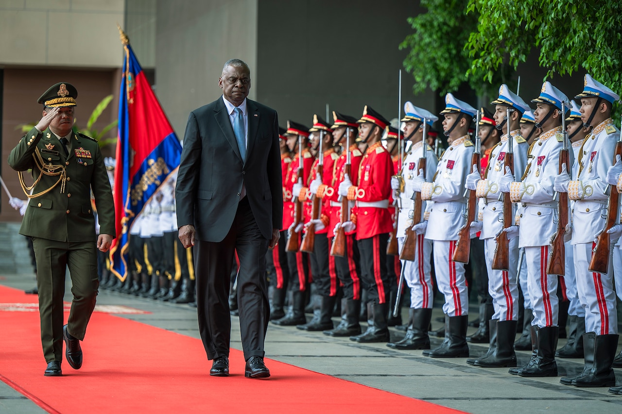 A person in business attire walks amid a row of military service members.