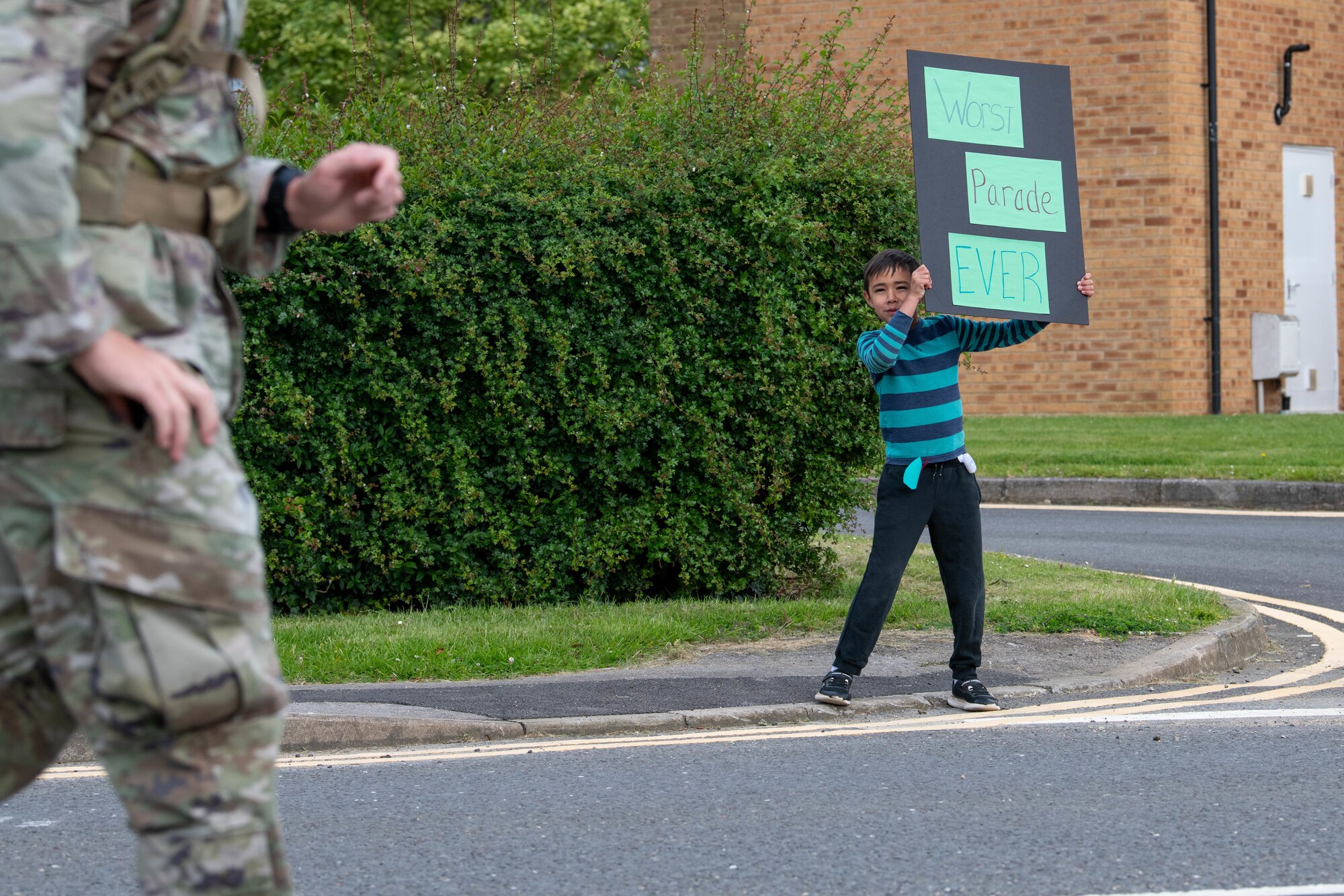 A young spectator cheers on participants with a “WORST PARADE EVER” sign