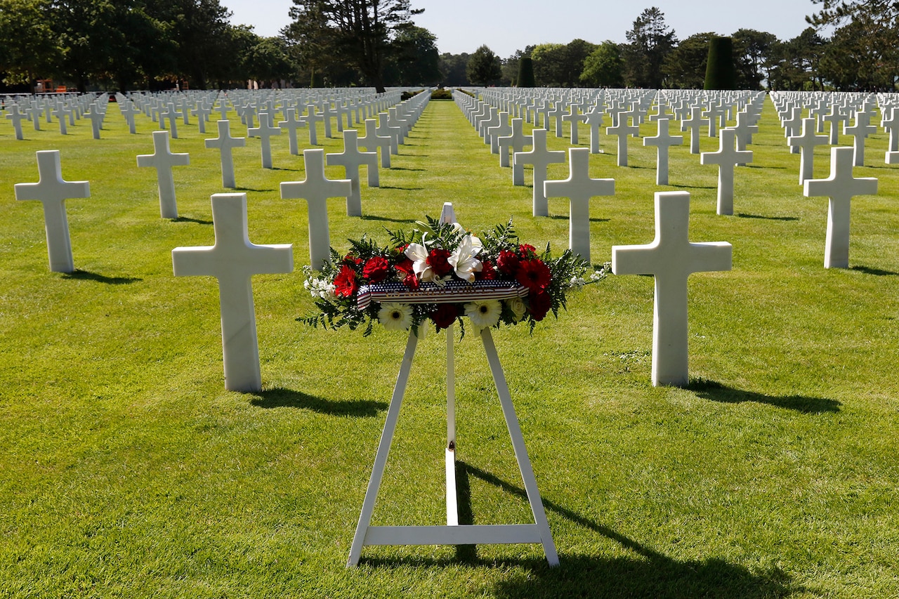 A wreath stands in a cemetery full of identical white crosses marking gravesites.