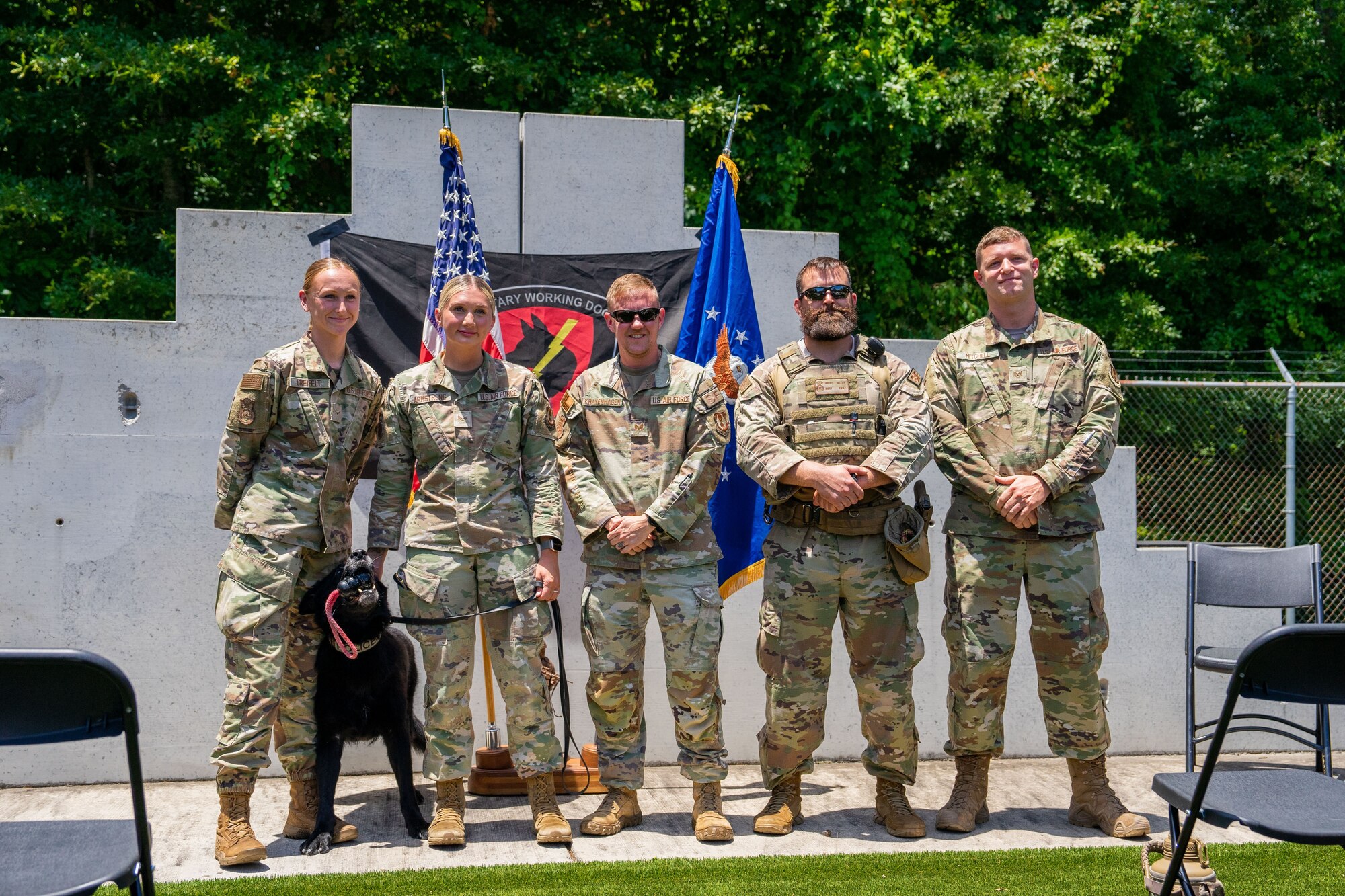 A group of people in military uniform and one military dog stand posing for a photo