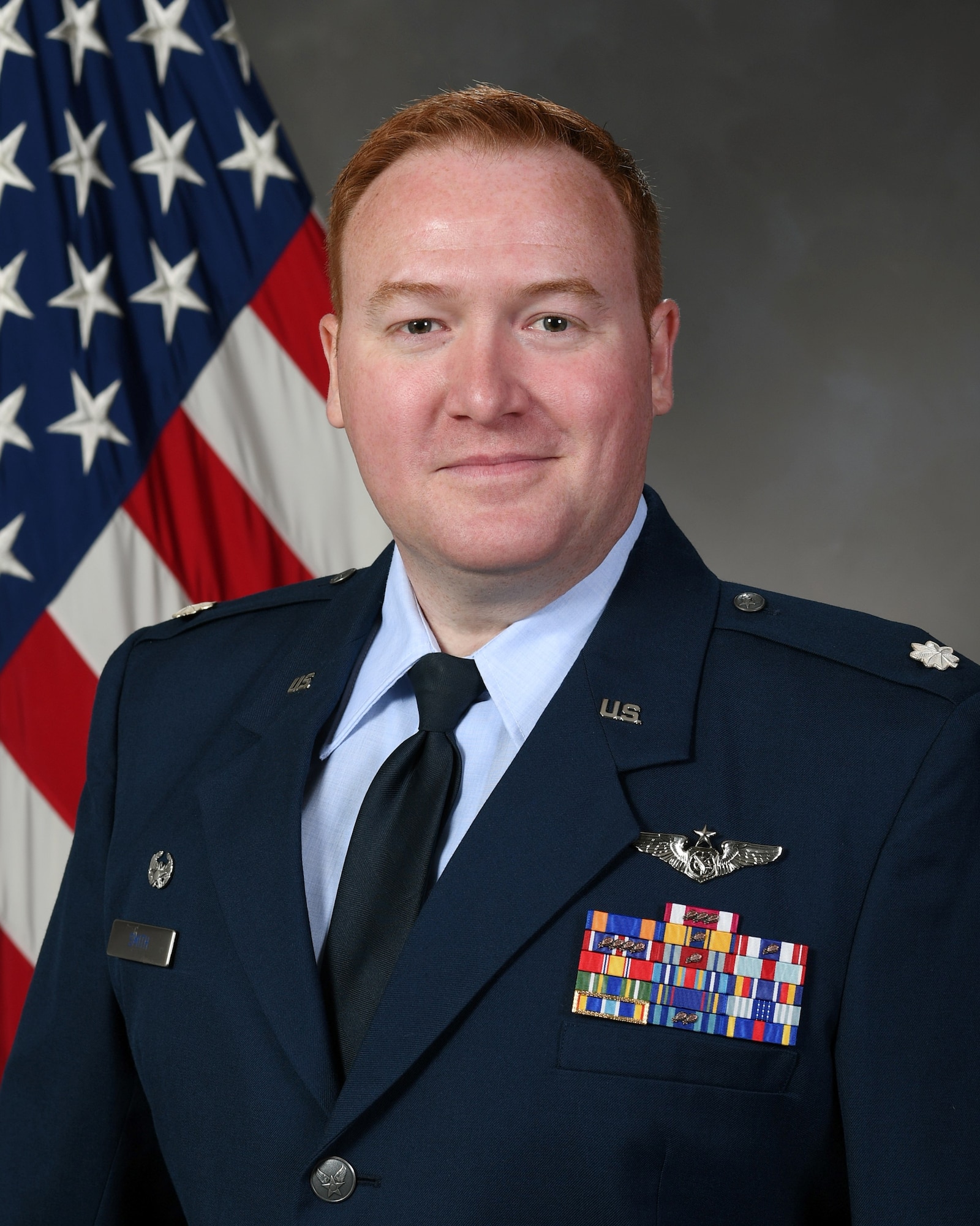 photo of uniformed U.S. Air Force Lt. Col. Ryan Smith wearing service dress uniform in front of a U.S. flag and gray background