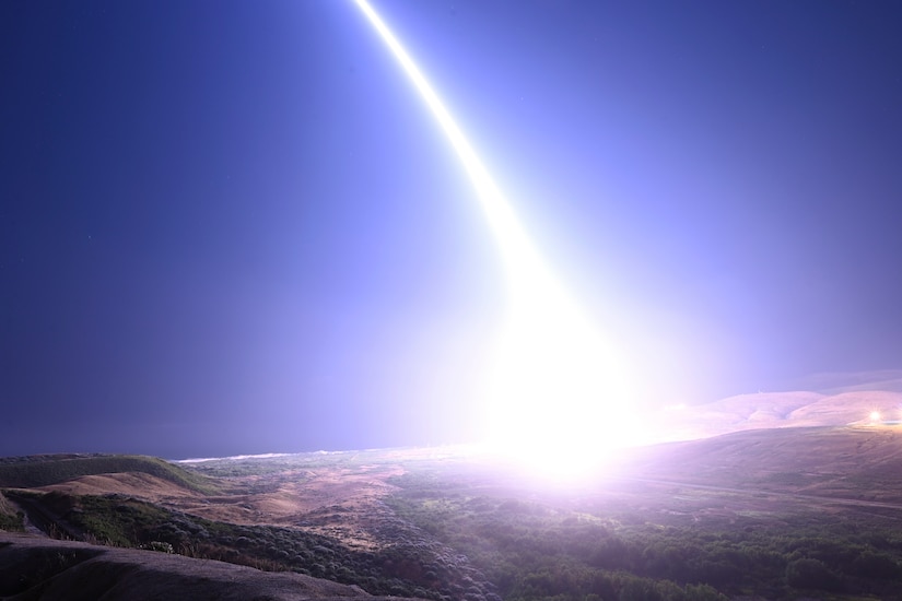 A launched missile illuminates mountainous terrain as it leaves a streak in the sky.