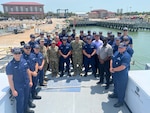 About 30 people in Coast Guard, military and civilian attire stand on the aft of a Coast Guard cutter.