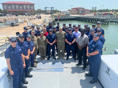 About 30 people in Coast Guard, military and civilian attire stand on the aft of a Coast Guard cutter.