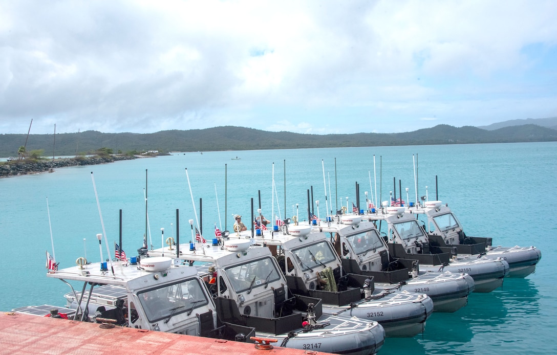 Six smaller grey military boats lined up at a pier