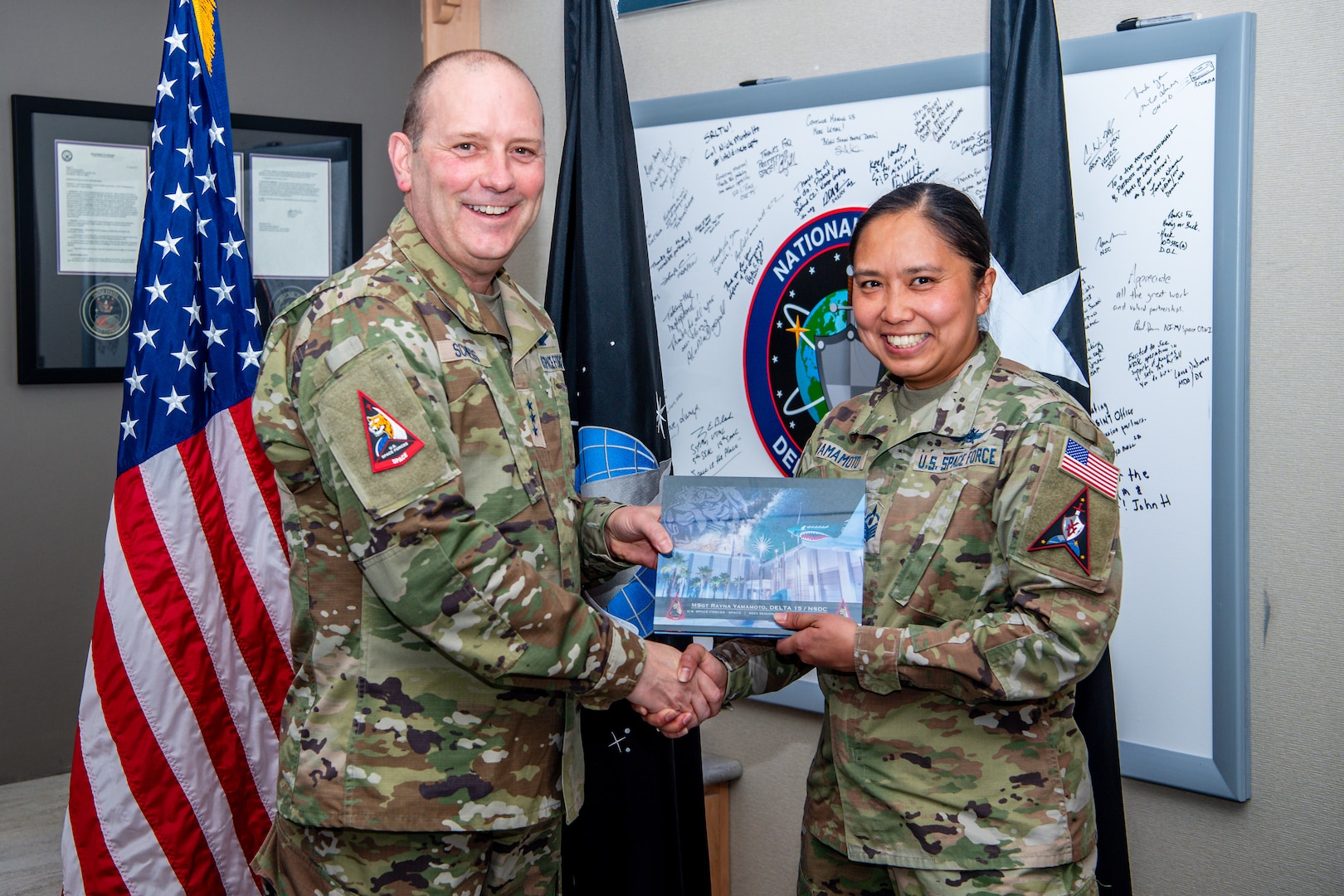 Two military members shaking hands and holding award plaque