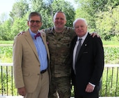 two male civilians pose with one male soldier after the change of command ceremony.