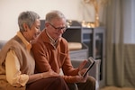 Elderly couple sits on couch and looks at a tablet device together.