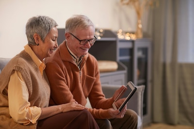Elderly couple sits on couch and looks at a tablet device together.