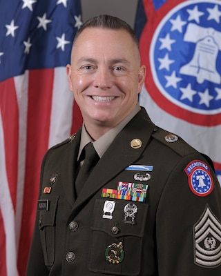 Male Soldier posed in front of the U.S. flag and the USAREC flag.