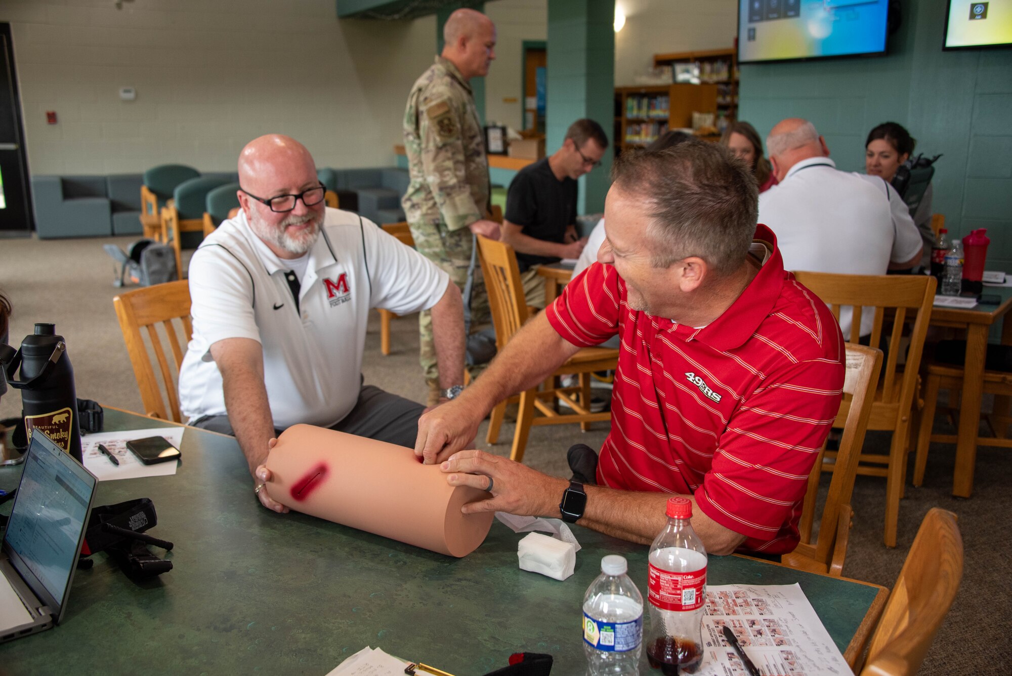 one man holds a simulated wound dummy while the other practices packing the wound