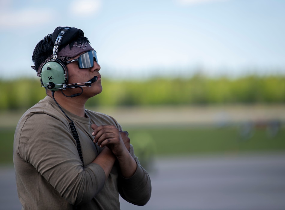 A maintainer poses with his arms crossed in front of his chest while marshalling a jet off the runway.
