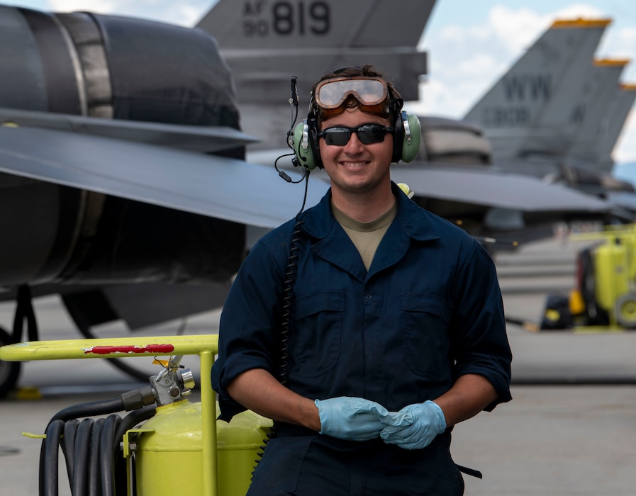 A maintainer stands and smiles for a photo in front some parked F-16s.