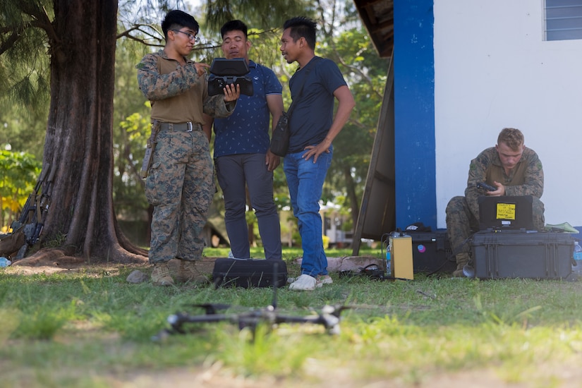 A Marine holds a device to show two Philippine marines while standing in the woods.
