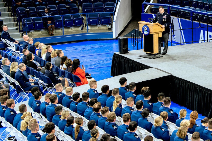 A person at a podium on stage speaks to dozens of seated cadets.