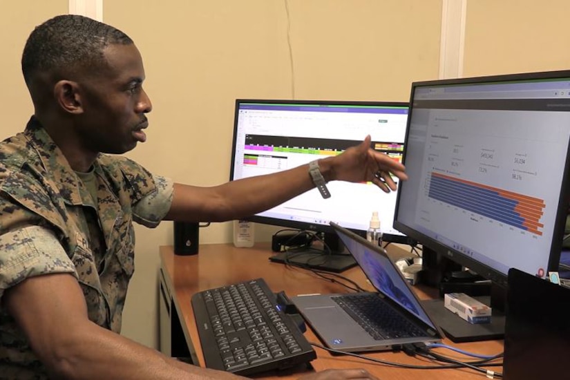 A Marine sits at a computer and gestures toward the monitor.