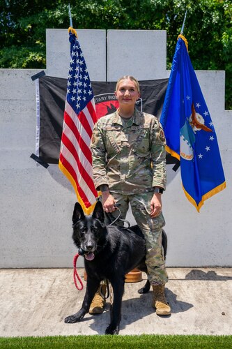 Woman in military uniform stands and poses with military dog
