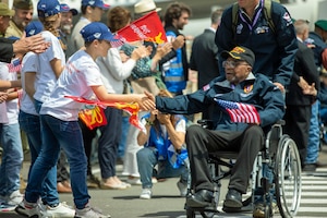 A veteran being pushed in a wheelchair shakes the hand of a child from dozens of people on the sidelines.