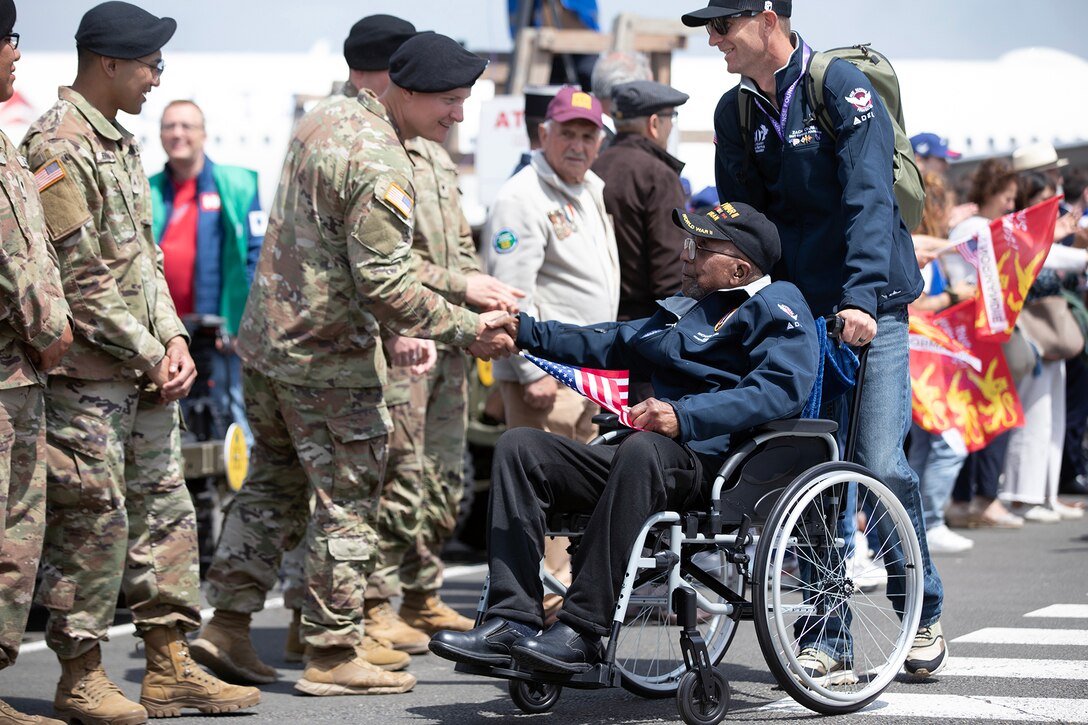 Soldiers shake hands with a veteran holding a U.S. flag on a flight line.