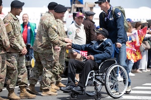 Soldiers shake hands with a veteran holding a U.S. flag on a flight line.