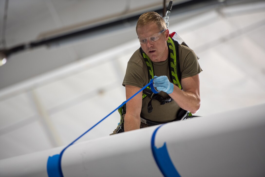 Tech. Sgt. Derek Clow, an aircraft structural repairman from the 123rd Maintenance Squadron, aligns masking tape to the wing of a C-130J Super Hercules aircraft while tethered to a safety harness prior to painting black and white stripes on the fuselage at the Kentucky Air National Guard Base in Louisville, Ky., May 14, 2024. The plane is scheduled to patriciate in D-Day observations in France on June 6 bearing the stripes, which were used to mark U.S. aircraft during World War II. (U.S. Air National Guard photo by Airman 1st Class Annaliese Billings)