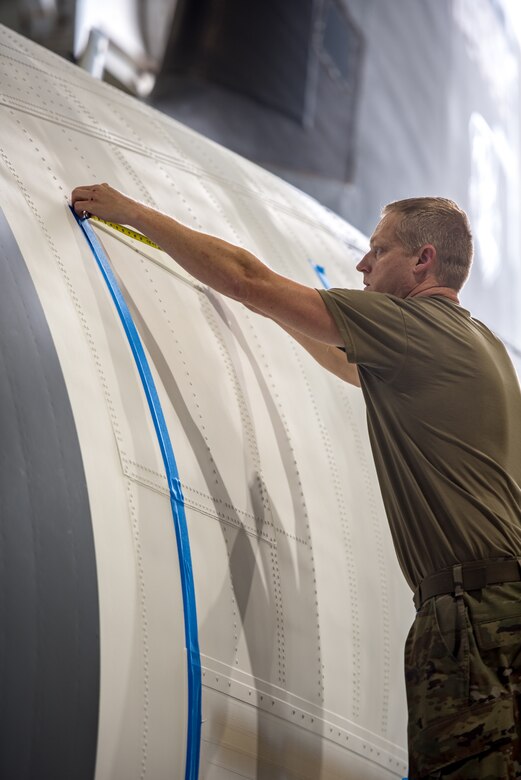 Tech. Sgt. Derek Clow, an aircraft structural craftsman from the 123rd Maintenance Squadron, aligns masking tape to the side of a Kentucky Air National Guard C-130J Super Hercules prior to painting black and white stripes on the aircraft in Louisville, Ky., May 14, 2024. The plane is scheduled to patriciate in D-Day observations in France on June 6 bearing the stripes, which were used to mark U.S. aircraft during World War II. (U.S. Air National Guard photo by Airman 1st Class Annaliese Billings)