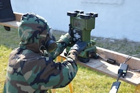 Warfighter in protective suit adjusts settings on a chemical vapor detector.