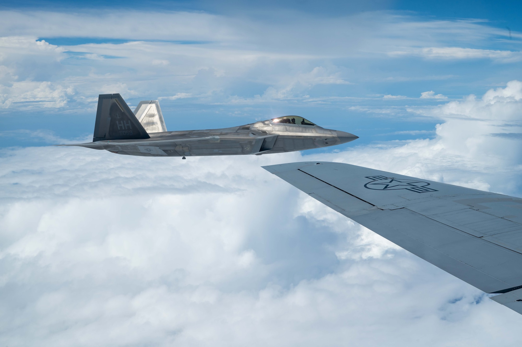 A U.S. Air Force F-22A Raptor operated by the 199th and 19th Fighter Squadrons flies alongside a KC-135 Stratotanker to conduct aerial refueling.
