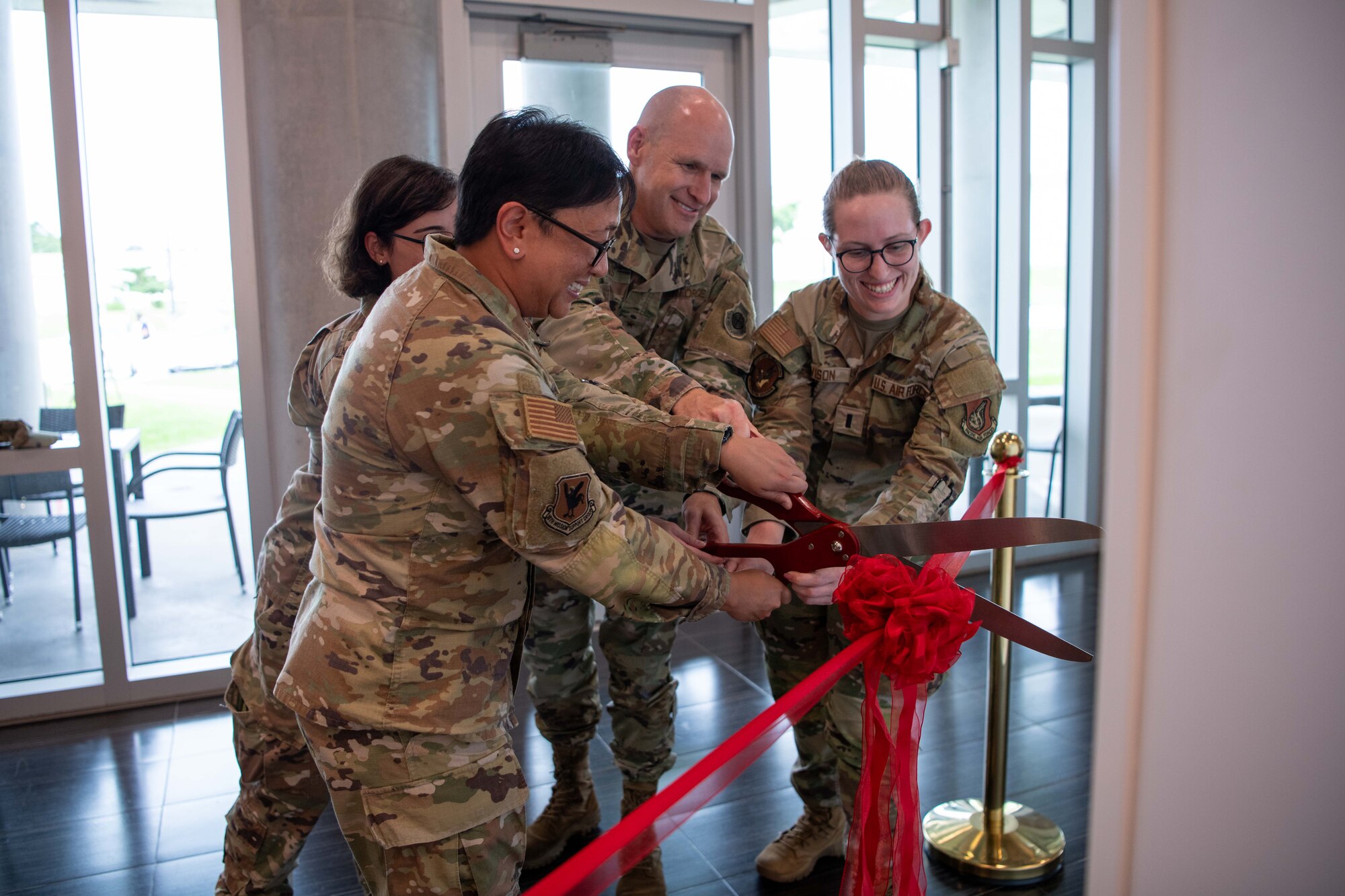 military members cut a ribbon with a big pair of scissors infront of a lactation pod for a photo