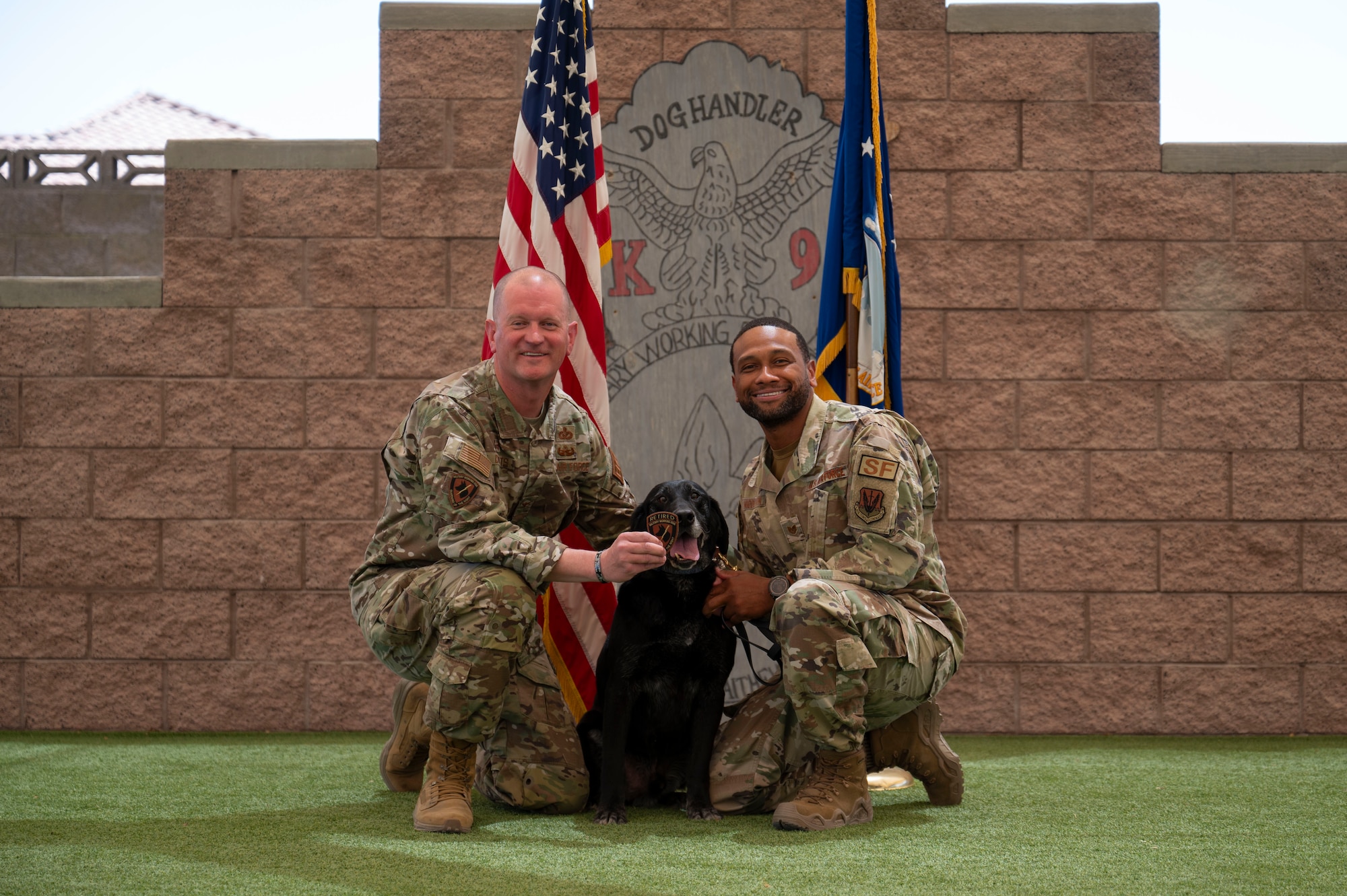 U.S. Air Force Col. Joshua DeMotts, left, 99th Air Base Wing commander, and Tech. Sgt. Albert Middleton, 99th Security Forces Squadron kennel master, present a military working dog (MWD) retirement patch to MWD Ivan during his retirement ceremony at Nellis Air Force Base, Nevada, May 23, 2024.