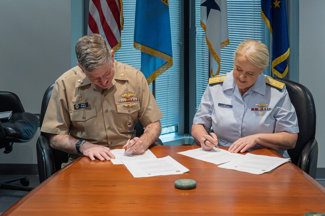 A man and a woman sit at a wooden table signing documents