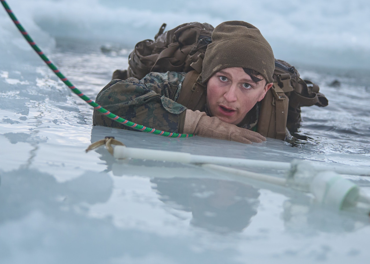 A service member crawls from frigid water onto ice.