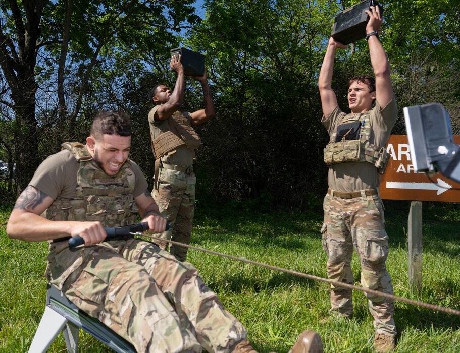 Two Airman push weights above their heads while a third works out on a rowing machine.