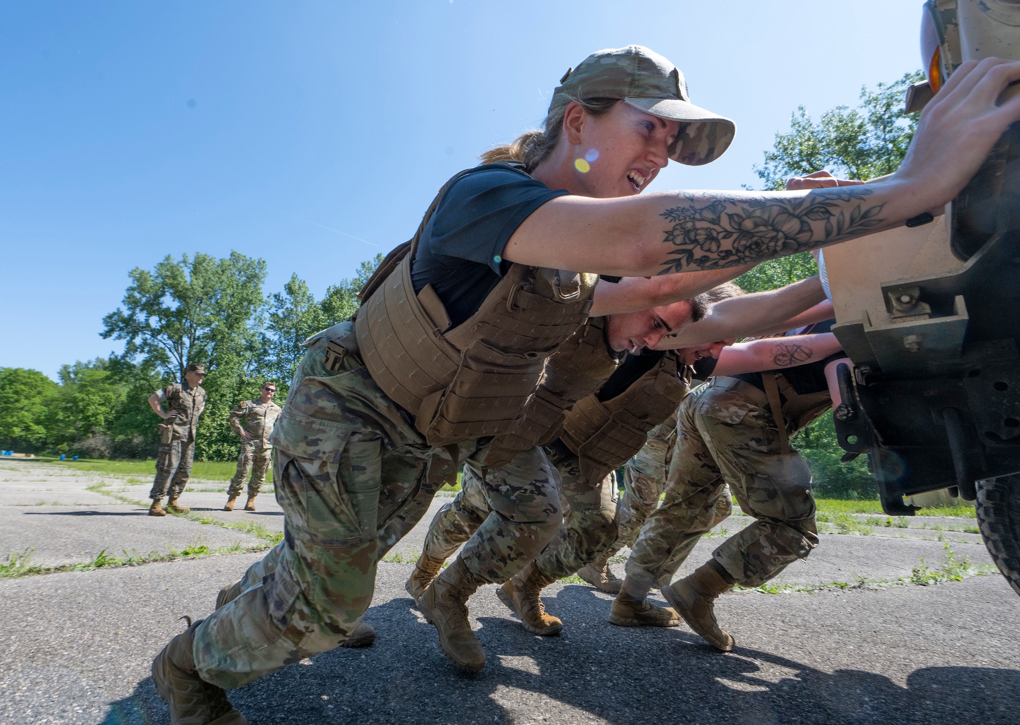 A low angle photo of a line of Airmen, with their feet dug into the ground, push against the back of a vehicle.