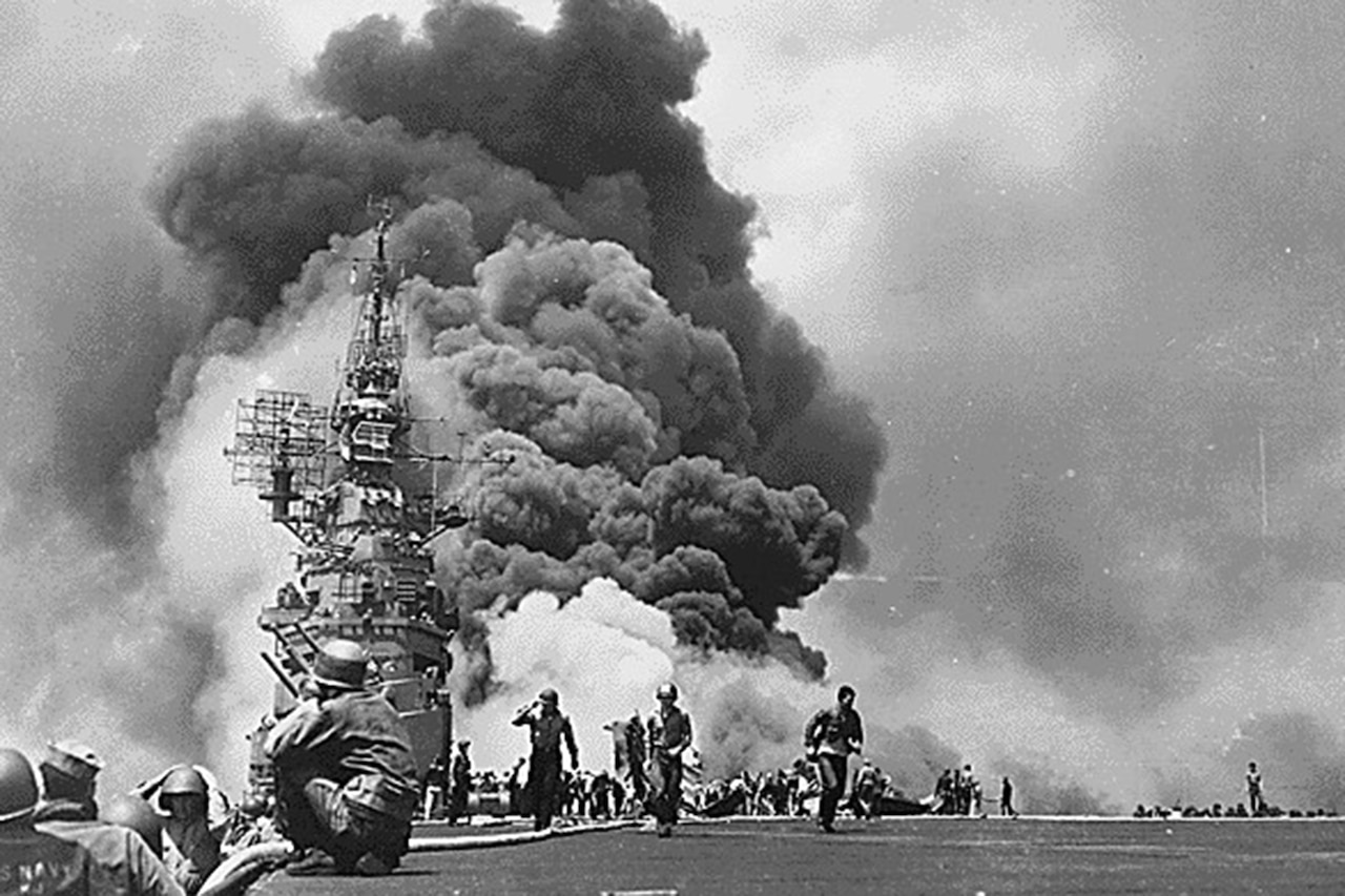 A ship billows thick, black smoke as men on a pier watch.