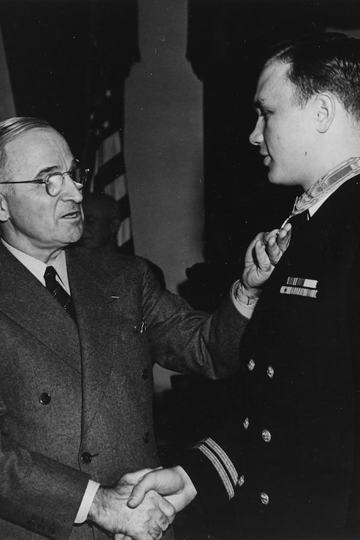 Two people shake hands as one holds a medal around the other man’s neck.