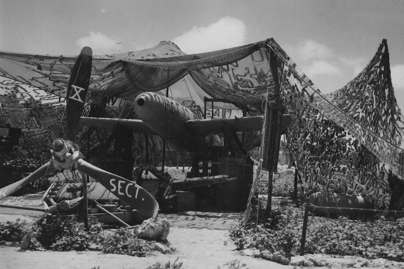 A propeller aircraft sits under shaded netting.