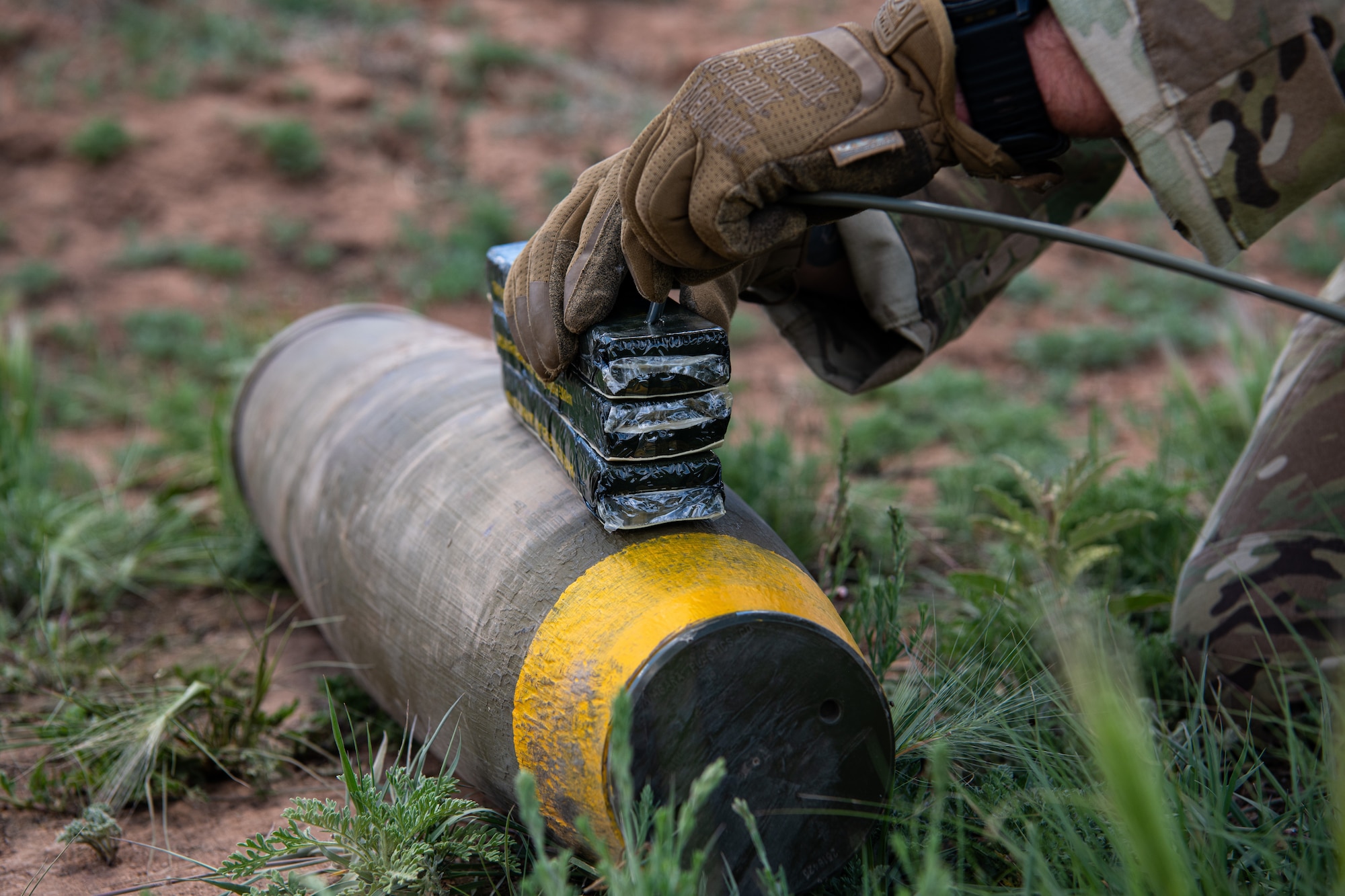 A man in military uniform places explosives on a piece of military ordnance.