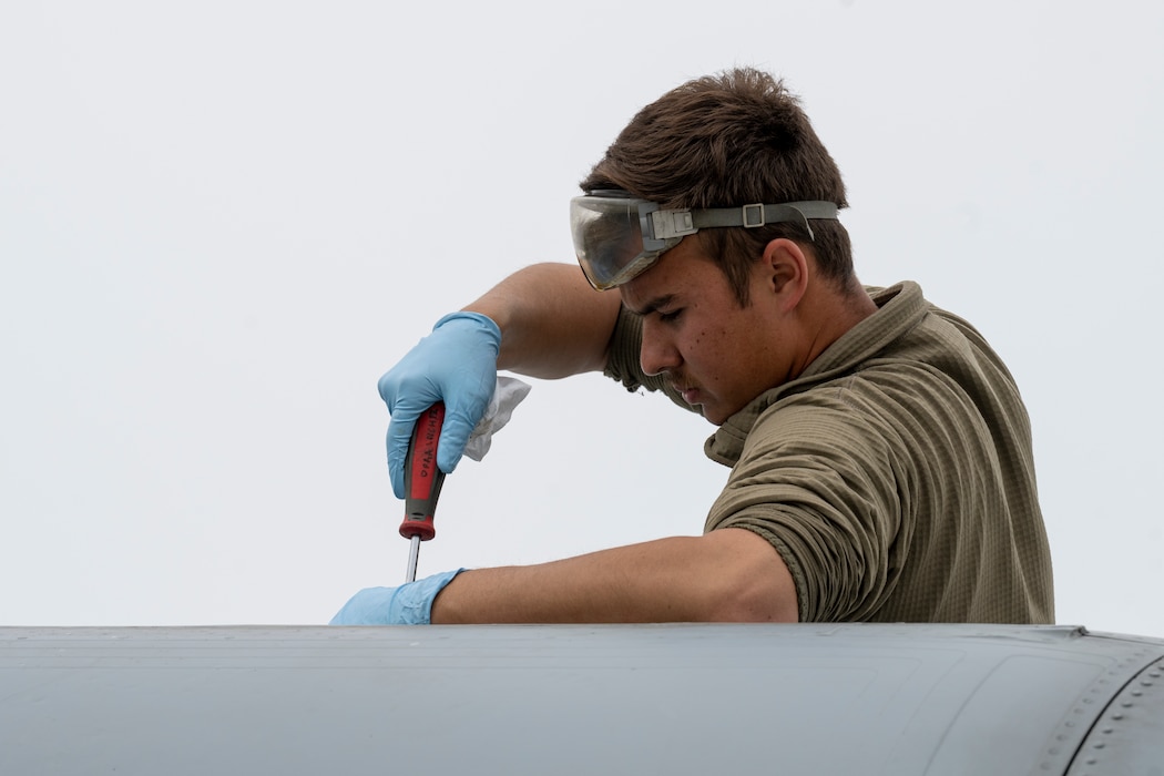 A maintainer uses a screwdriver to screw in screws on an A-10 aircraft.