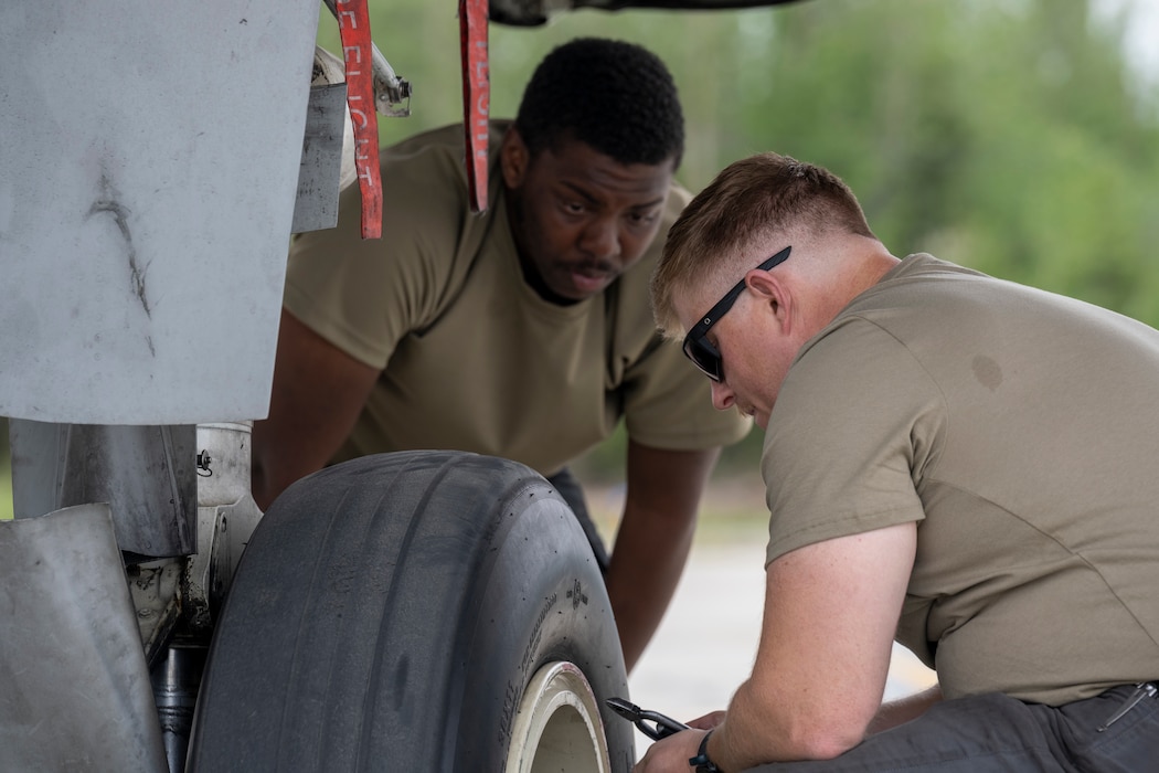 Two men work together to replace a tire on an A-10 aircraft.