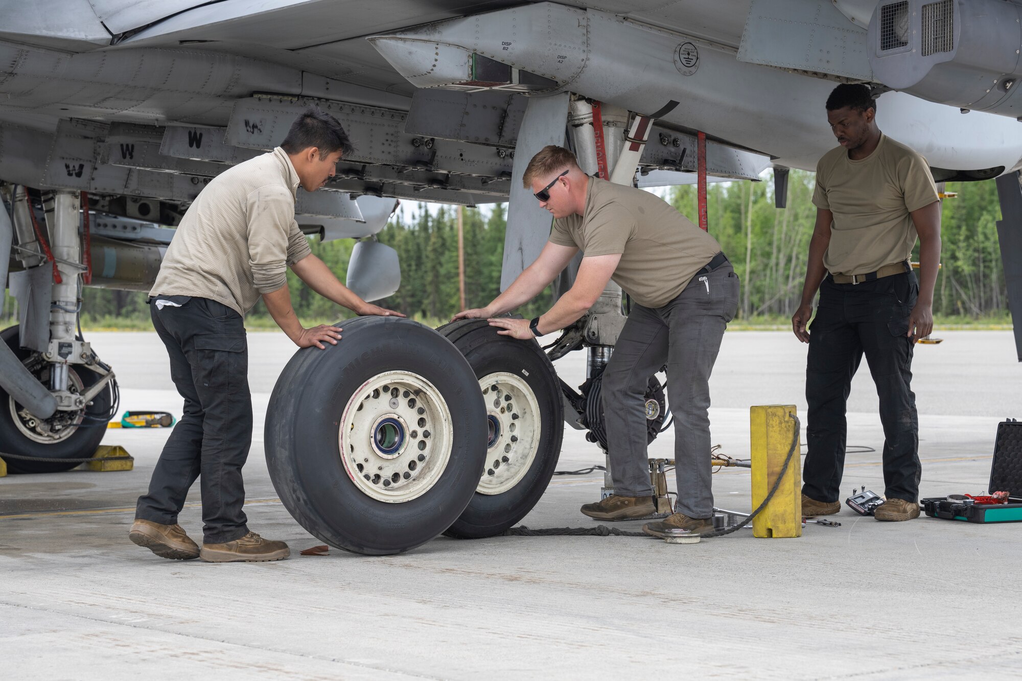 The man on the left pushes the new tire forward while the man in the middle pushes the old tire back. The third man on the right acts a spotter.