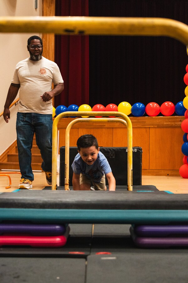 Lee Haynes, left, the Camp Hansen fitness coordinator with Marine Corps Community Services, guides a child through an obstacle course during the 2024 Ages and Stages community event outside the Camp Foster Community Center on Okinawa, Japan, May 18, 2024. The MCCS New Parent Support branch hosted the event to showcase available parental resources, including parenting classes, briefings, and home visitations. Haynes is a native of New Mexico. (U.S. Marine Corps photo by Cpl. Jonathan Beauchamp)