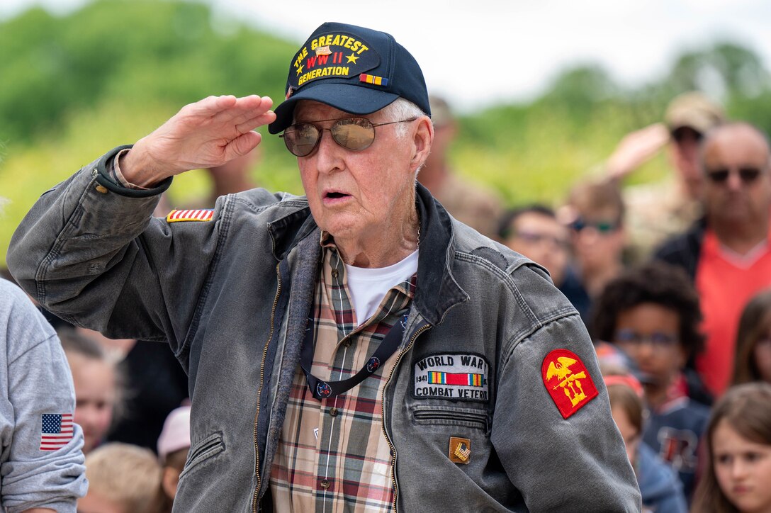 A person in civilian clothes and a WWII “The Greatest Generation” cap salutes.
