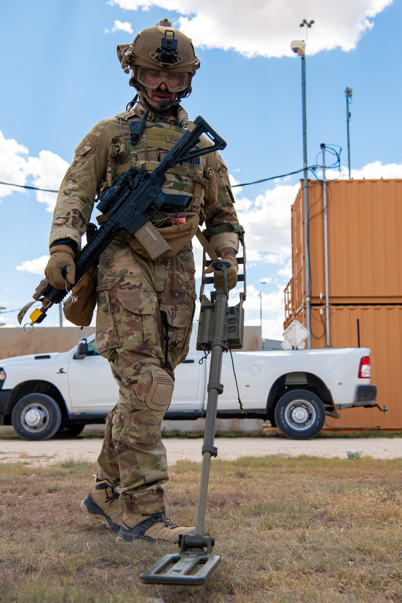 A man in military uniform and military equipment uses a metal detector.