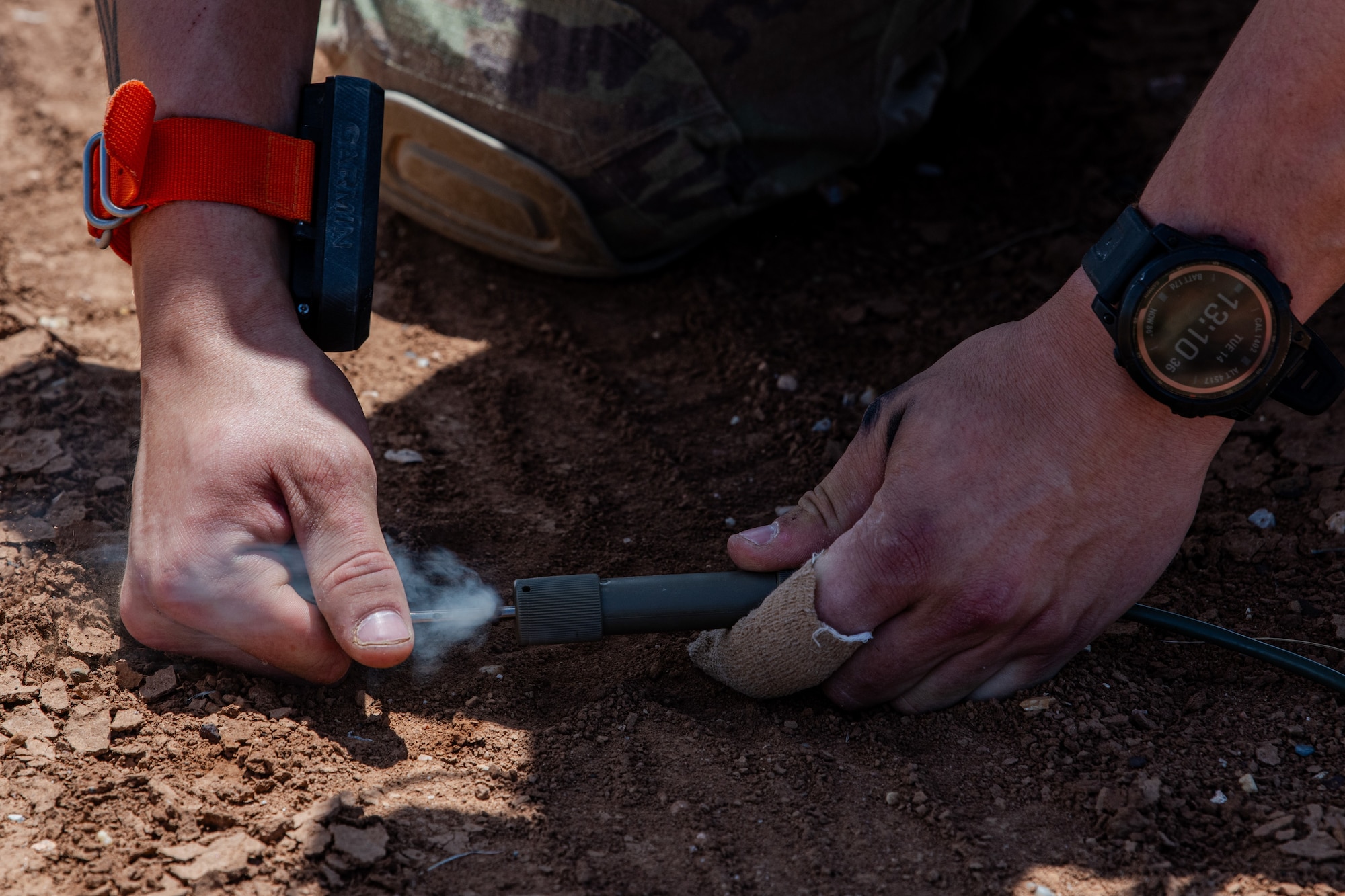 A man manipulates military equipment laying on the ground.