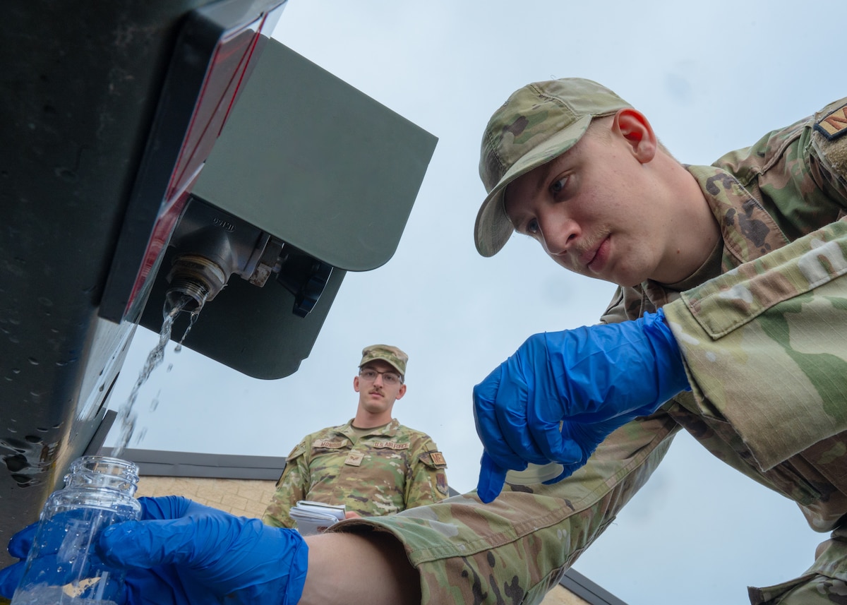 a bioenvironmental engineering technician takes a water sample from a potable water tank