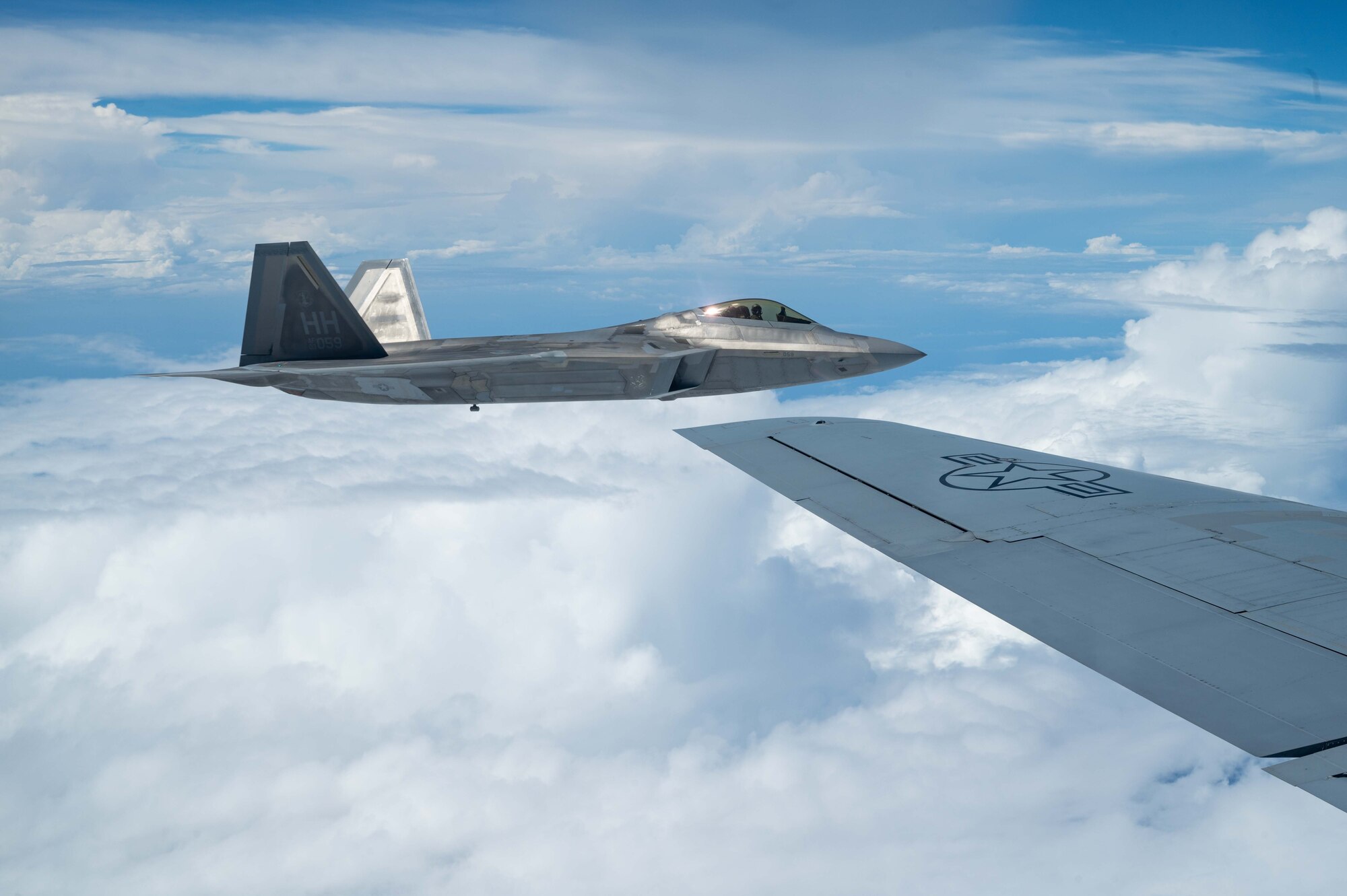 A U.S. Air Force F-22A Raptor operated by the 199th and 19th Fighter Squadrons flies alongside a KC-135 Stratotanker to conduct aerial refueling.