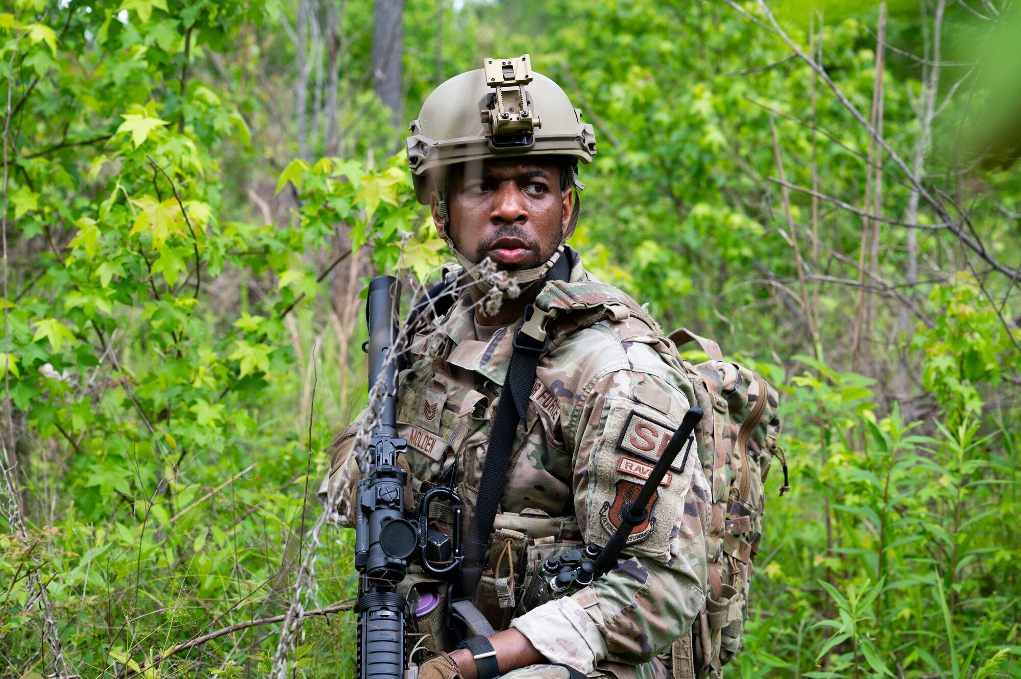 An Airman stands in a field with his kit and rifle.