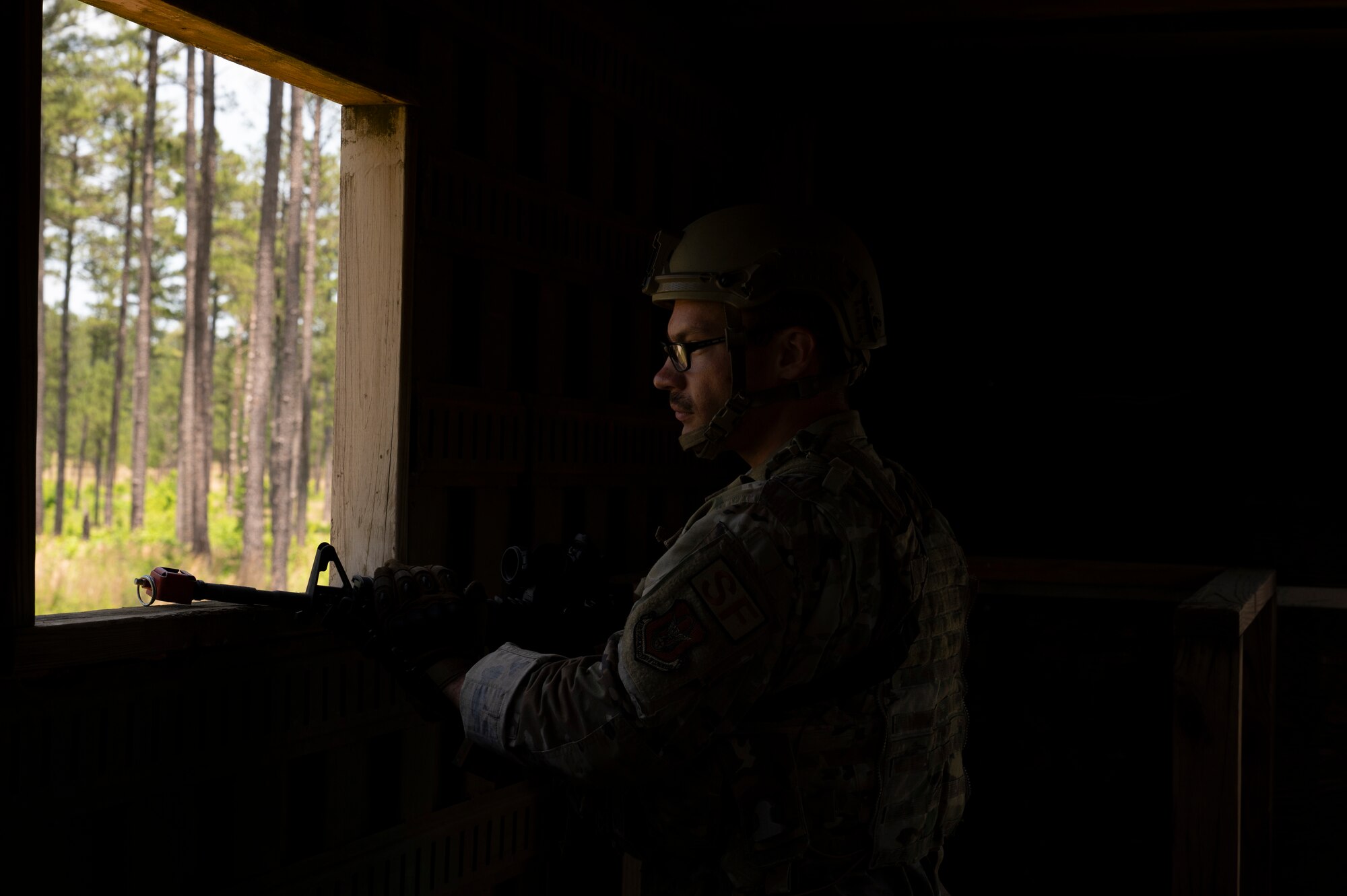 An Airman looks out of a window with his rifle.